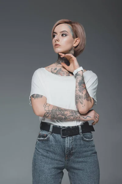 Красива молода жінка з татуюваннями дивиться ізольовано на сірому — стокове фото