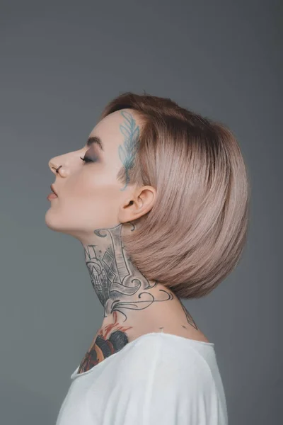 Retrato de perfil de hermosa chica tatuada con los ojos cerrados aislados en gris - foto de stock