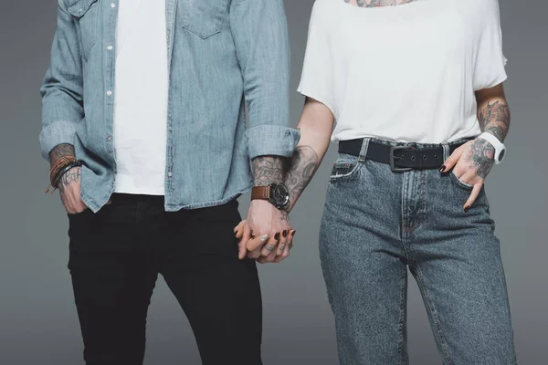 Abgeschnittene Aufnahme von stylischem jungen tätowierten Paar, das die Hände isoliert auf grau hält — Stockfoto