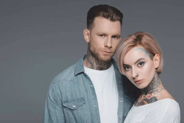 Portrait of beautiful stylish young couple with tattoos looking at camera isolated on grey — Stock Photo