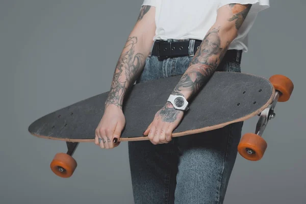 Mid section of girl with tattoos holding skateboard isolated on grey — Stock Photo