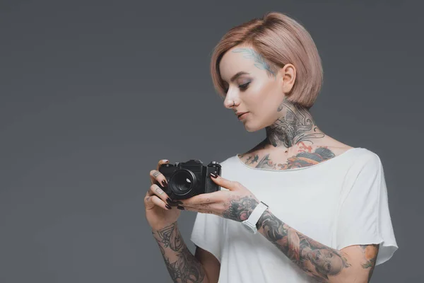 Hermosa chica con tatuajes celebración cámara aislada en gris - foto de stock