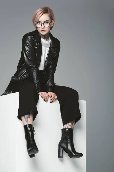 Stylish young woman with tattoos wearing leather jacket and looking at camera isolated on grey — Stock Photo