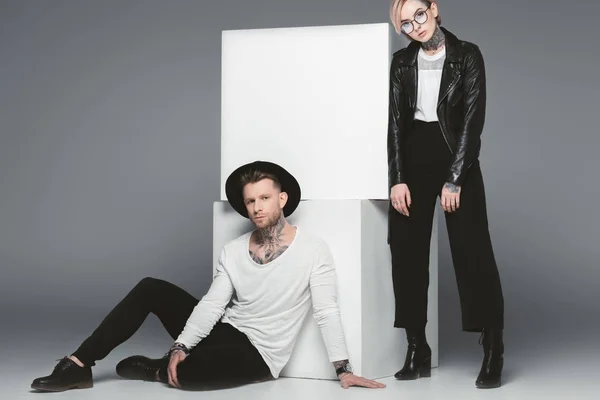 Fashionable tattooed couple posing near white cubes, isolated on grey — Stock Photo