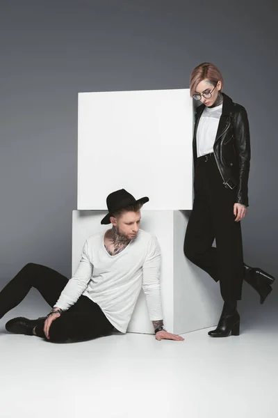 Stylish tattooed couple posing near white cubes, isolated on grey — Stock Photo