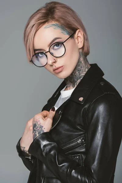 Belle fille tatouée en lunettes et veste en cuir noir, isolée sur gris — Photo de stock