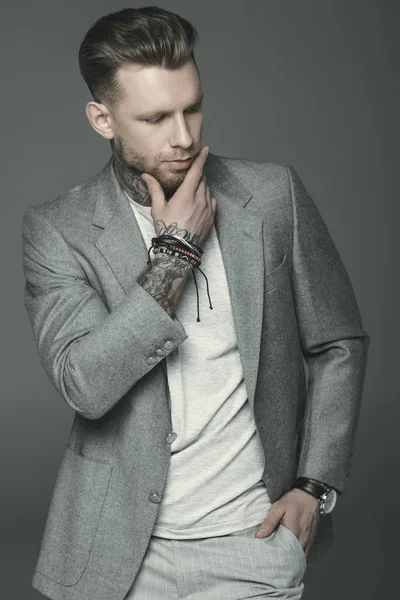 Hombre de negocios tatuado pensativo en traje gris, aislado en gris - foto de stock