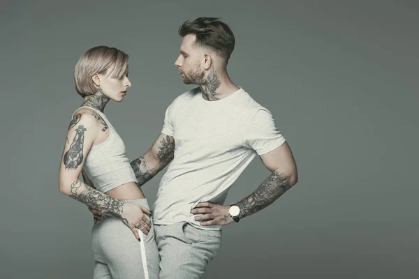 Pareja tatuada de moda en ropa deportiva posando juntos, aislados en gris - foto de stock