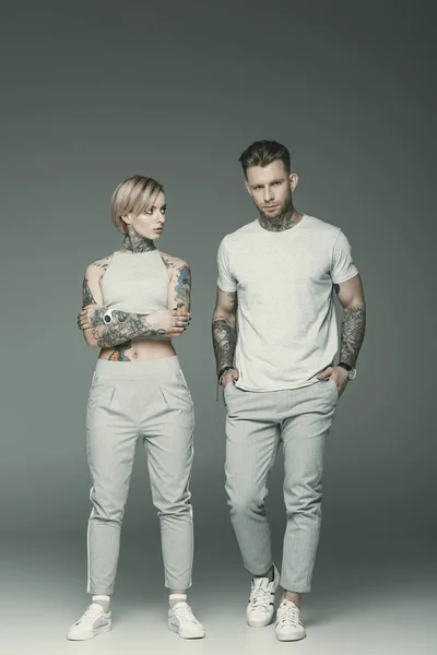 Beautiful tattooed couple in sportswear posing together, isolated on grey — Stock Photo