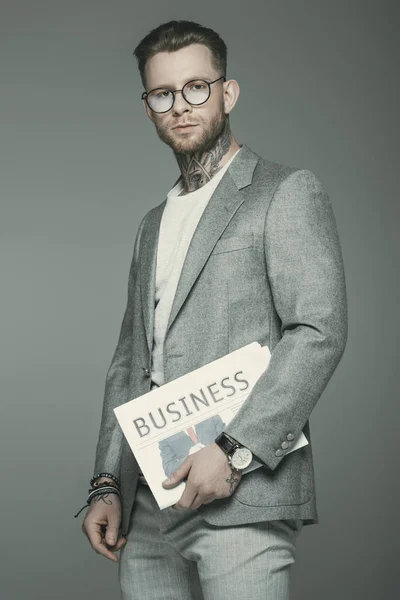 Stylish businessman in eyeglasses and suit holding business newspaper, isolated on grey — Stock Photo