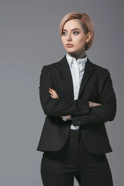 Tattooed businesswoman posing in suit with crossed arms, isolated on grey — Stock Photo