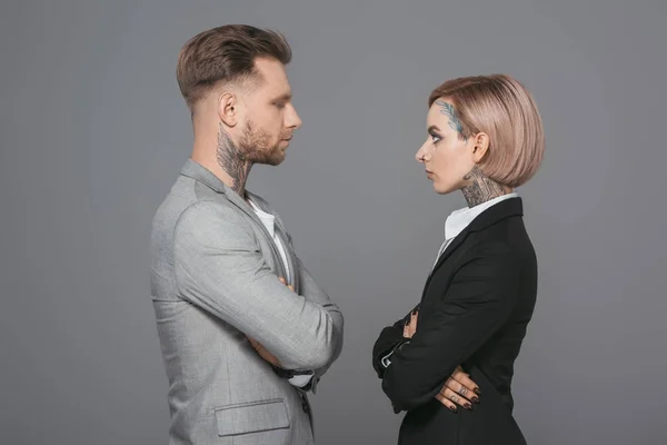 Homem de negócios elegante e mulher de negócios com braços cruzados olhando um para o outro, isolado em cinza — Fotografia de Stock