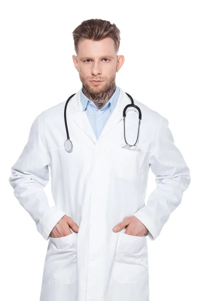 Médico profesional con estetoscopio y manos en bolsillos de bata blanca, aislado en blanco - foto de stock