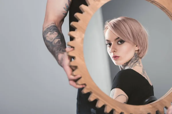 Tattooed man holding mirror with reflection of his beautiful girlfriend, isolated on grey — Stock Photo