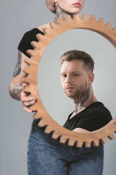 Mädchen hält Spiegel mit Reflexion ihres hübschen Freundes, isoliert auf grau — Stockfoto