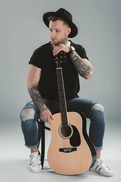 Guitarrista tatuado de moda en sombrero negro con guitarra acústica, aislado en gris - foto de stock