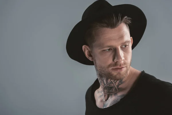 Модний татуйований чоловік в чорному капелюсі, ізольований на сірому — стокове фото