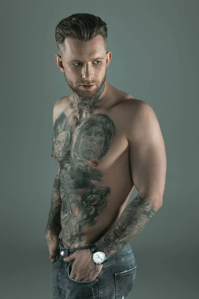 Hombre guapo sin camisa tatuado con las manos en los bolsillos, aislado en gris - foto de stock