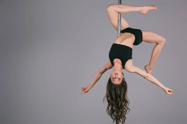 Upside down of beautiful sporty girl exercising with pole and looking at camera on grey — Stock Photo