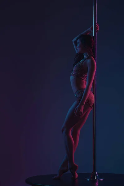 Side view of sporty seductive girl leaning at pole and looking away on blue — Stock Photo