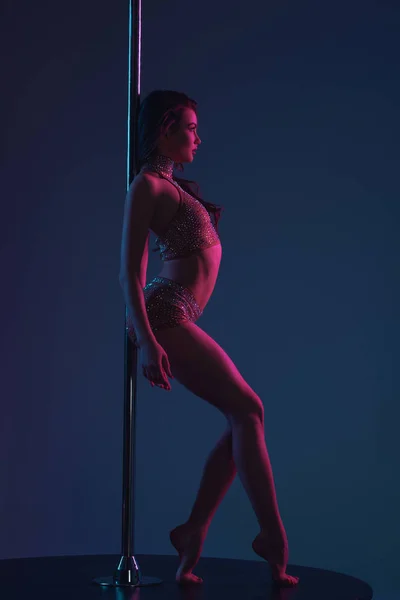 Side view of seductive sporty girl leaning at pole and looking away on blue — Stock Photo