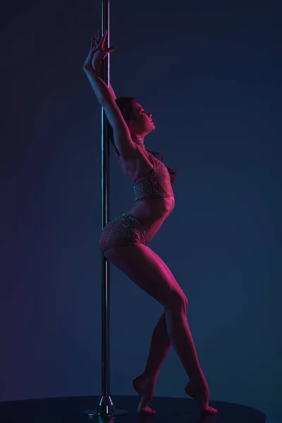 Seitenansicht der verführerischen jungen Tänzerin, die sich an eine Stange auf blau lehnt — Stockfoto