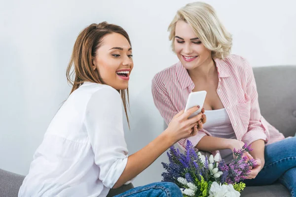 Красиві друзі-жінки сміються і використовують смартфон — стокове фото