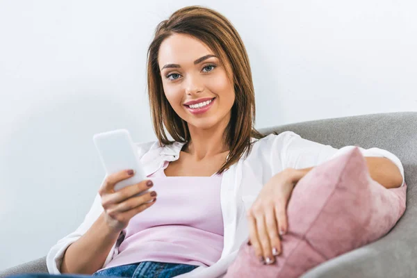 Cheerful beautiful woman using smartphone and sitting on armchair — Stock Photo