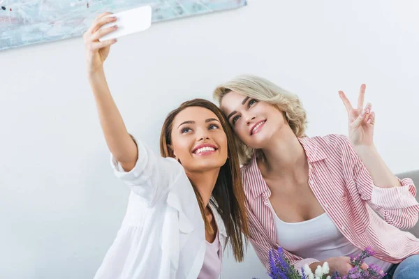 Cheerful female friends with victory sign taking selfie on smartphone — Stock Photo