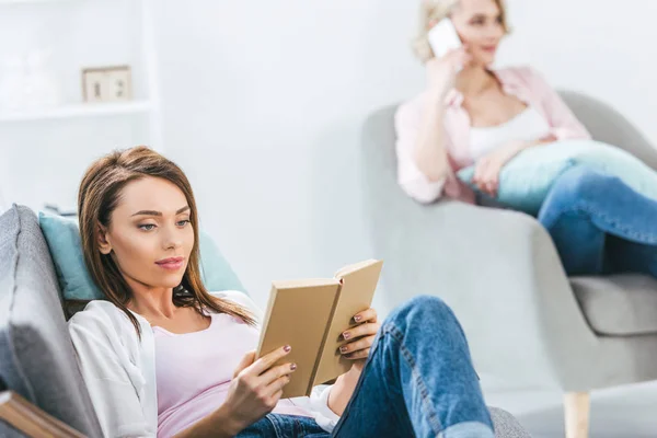 Amigas leyendo libro y usando smartphone - foto de stock