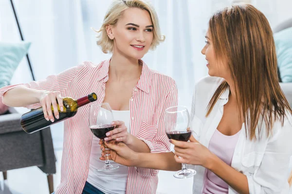 Atractivas mujeres sonrientes con vino tinto pasando tiempo juntas - foto de stock