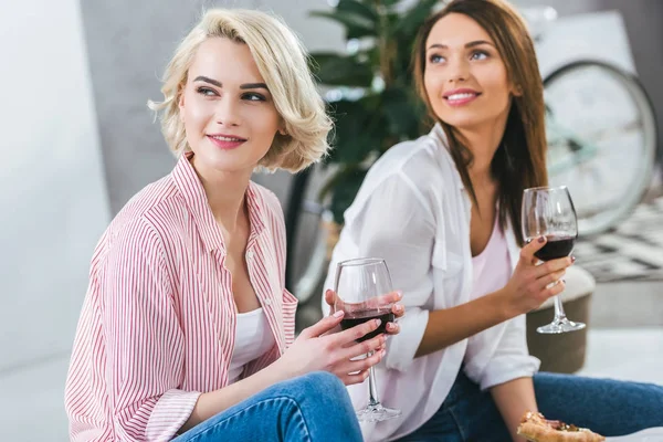 Atractivas mujeres sonrientes con vino tinto pasando tiempo juntas - foto de stock