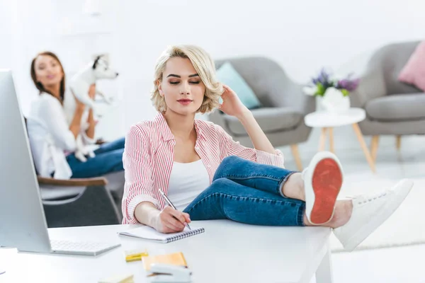 Hermosa chica escribiendo en bloc de notas mientras su amigo jugando con jack russell terrier perro - foto de stock