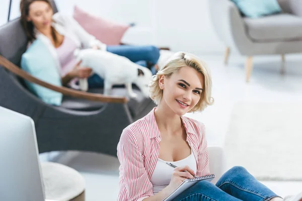 Sorrindo menina escrevendo no bloco de notas, enquanto seu amigo brincando com Jack Russell cão terrier — Fotografia de Stock