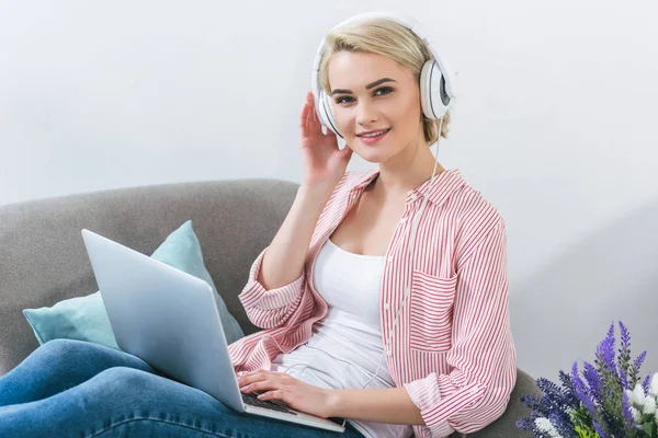 Красивая блондинка слушает музыку с наушниками и с помощью ноутбука — стоковое фото