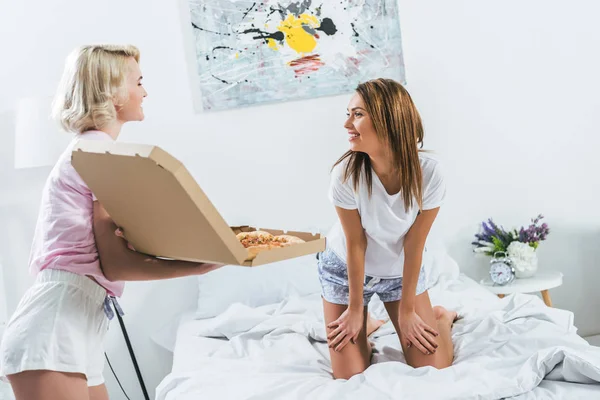 Beautiful girls spending time together and eating pizza in bed — Stock Photo