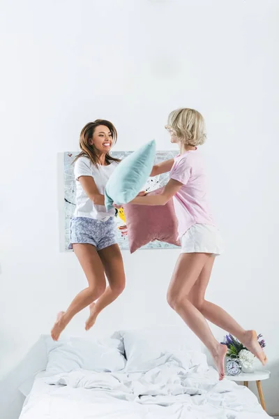 Beautiful girls jumping and having pillow fight on bed — Stock Photo