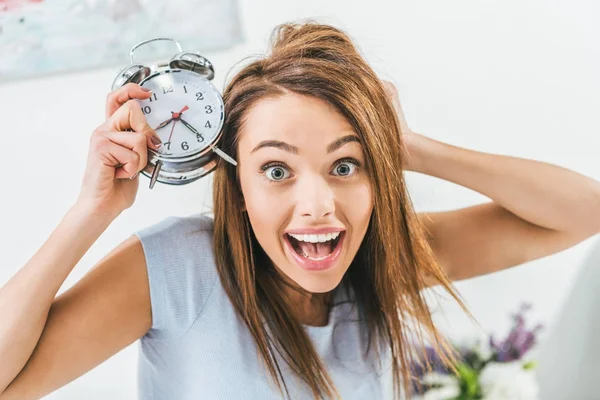 Aufgeregtes Mädchen mit Wecker und Blick in die Kamera — Stockfoto