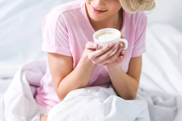 Vue recadrée de fille avec tasse de café assis sur le lit le matin — Photo de stock