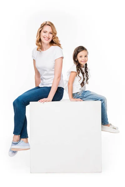 Mãe e filha sentados no cubo branco vazio isolado no branco — Fotografia de Stock