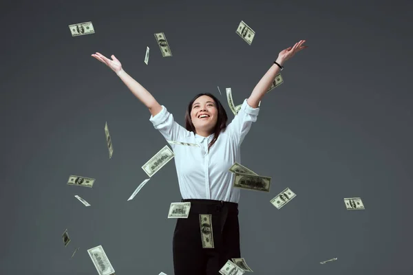 Happy young asian woman throwing dollar banknotes isolated on grey — Stock Photo