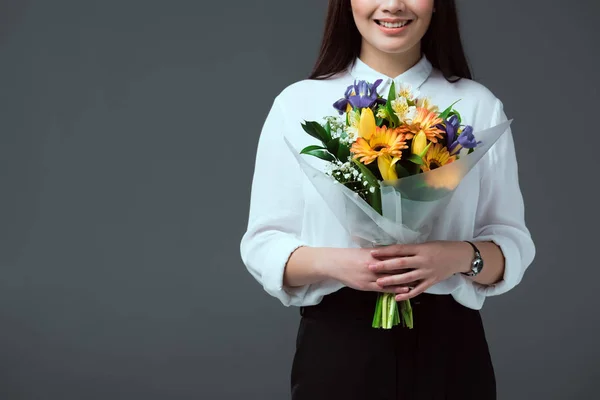Обрізаний знімок усміхненої молодої жінки, що тримає букет квітів ізольовано на сірому — стокове фото