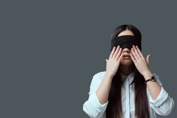 Young woman in black blindfold touching face with hands isolated on grey — Stock Photo
