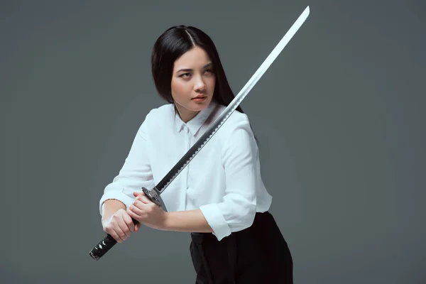 Красива азіатська дівчина тримає меч катани і дивиться ізольовано на сірому — стокове фото