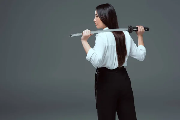 Back view of beautiful asian girl holding katana on shoulders isolated on grey — Stock Photo