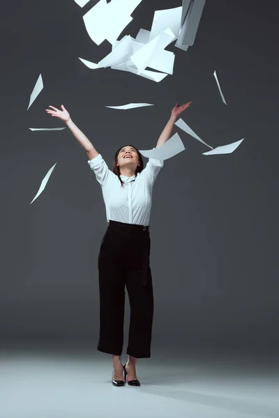 Повний вигляд щасливої молодої бізнес-леді кидає папери на сірий — стокове фото