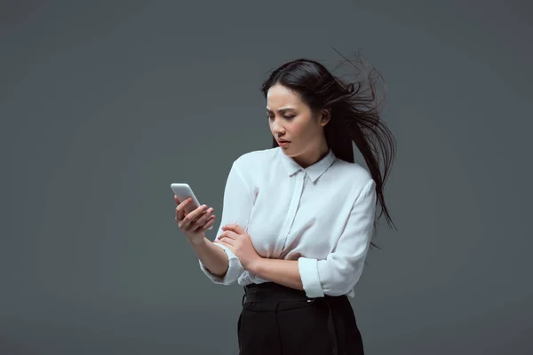 Ernsthafte junge asiatische Frau mit Smartphone isoliert auf grau — Stockfoto