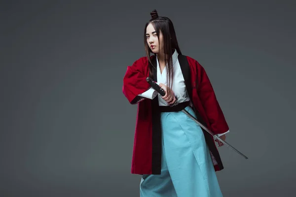 Asian woman in kimono holding katana sword and looking at camera isolated on grey — Stock Photo