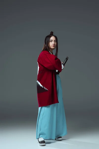 Jeune femme asiatique en kimono tenant katana épée et regardant caméra sur gris — Photo de stock