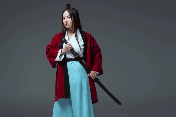 Junge asiatische Frau im Kimono mit Katana-Schwert und Blick auf Kamera isoliert auf grau — Stockfoto